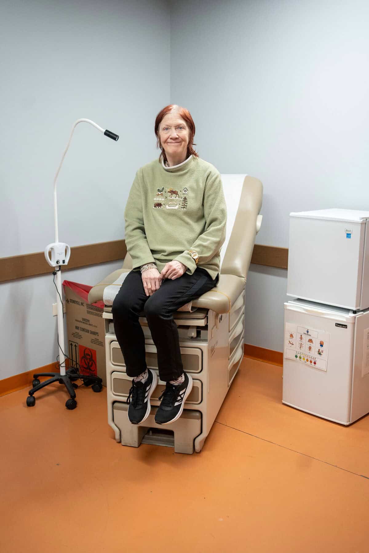 A woman sits in a medical office, smiling
