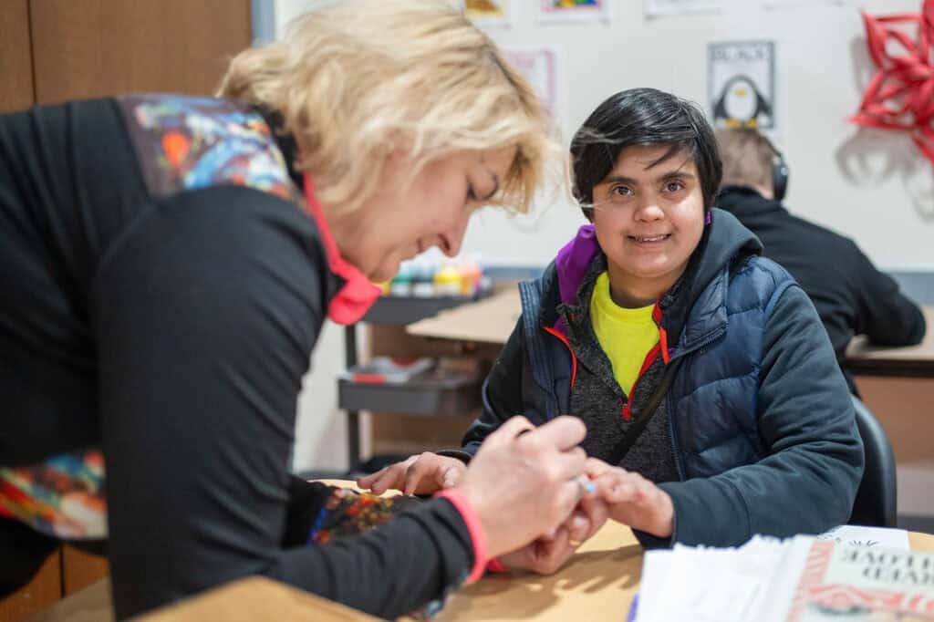 woman painting another woman's nails in a classroom setting