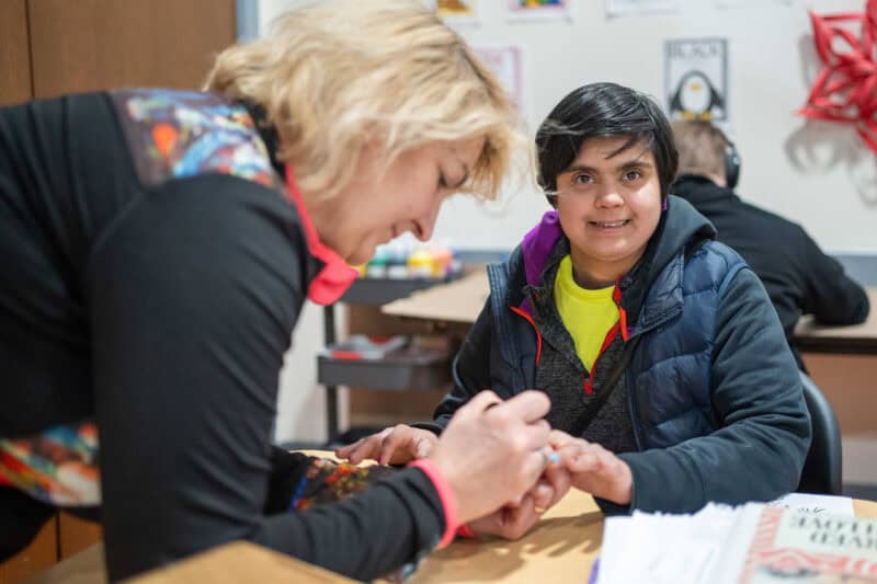 woman painting another woman's nails in a classroom setting