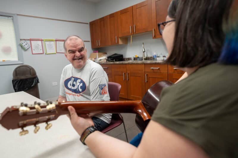 A man listens as a woman plays guitar