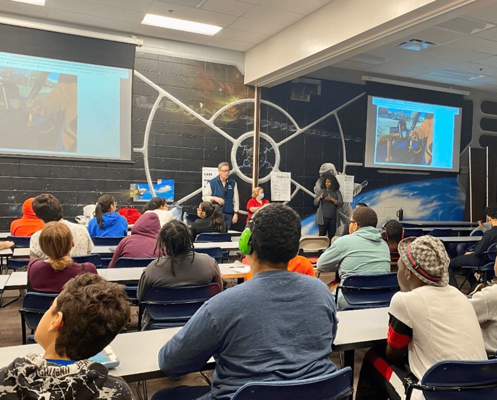 A man and two women presenting to a classroom of people