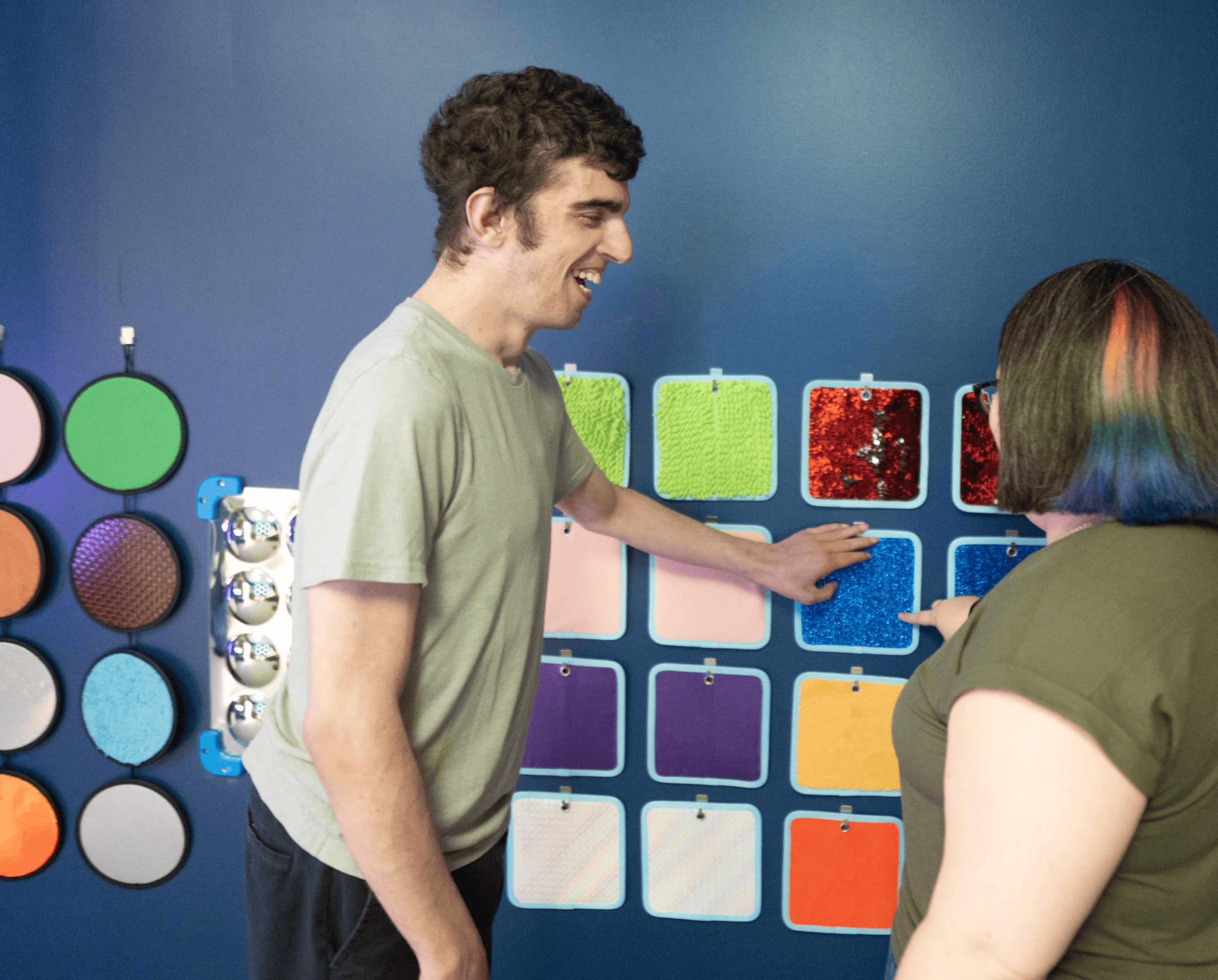 A man and woman stand in a blue room touching a sparkly blue square