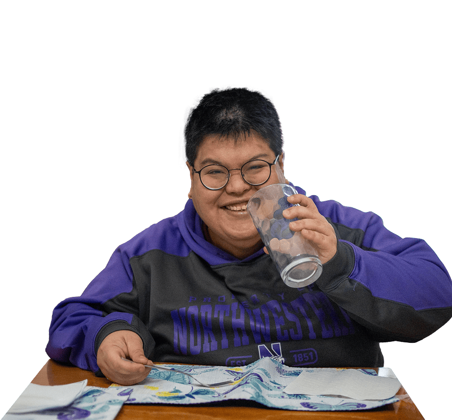 A person in a sweatshirt and glasses smiling, holding a drinking glass up to their face