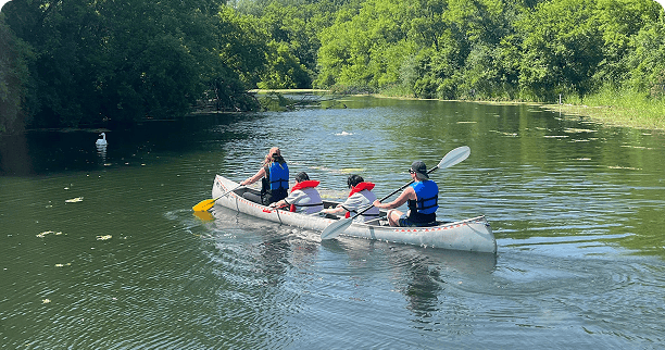 4 people rowing a canoe on a river surrounded by trees