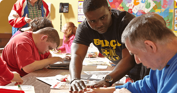 Classroom setting, a teacher standing next to another adult assisting with a project