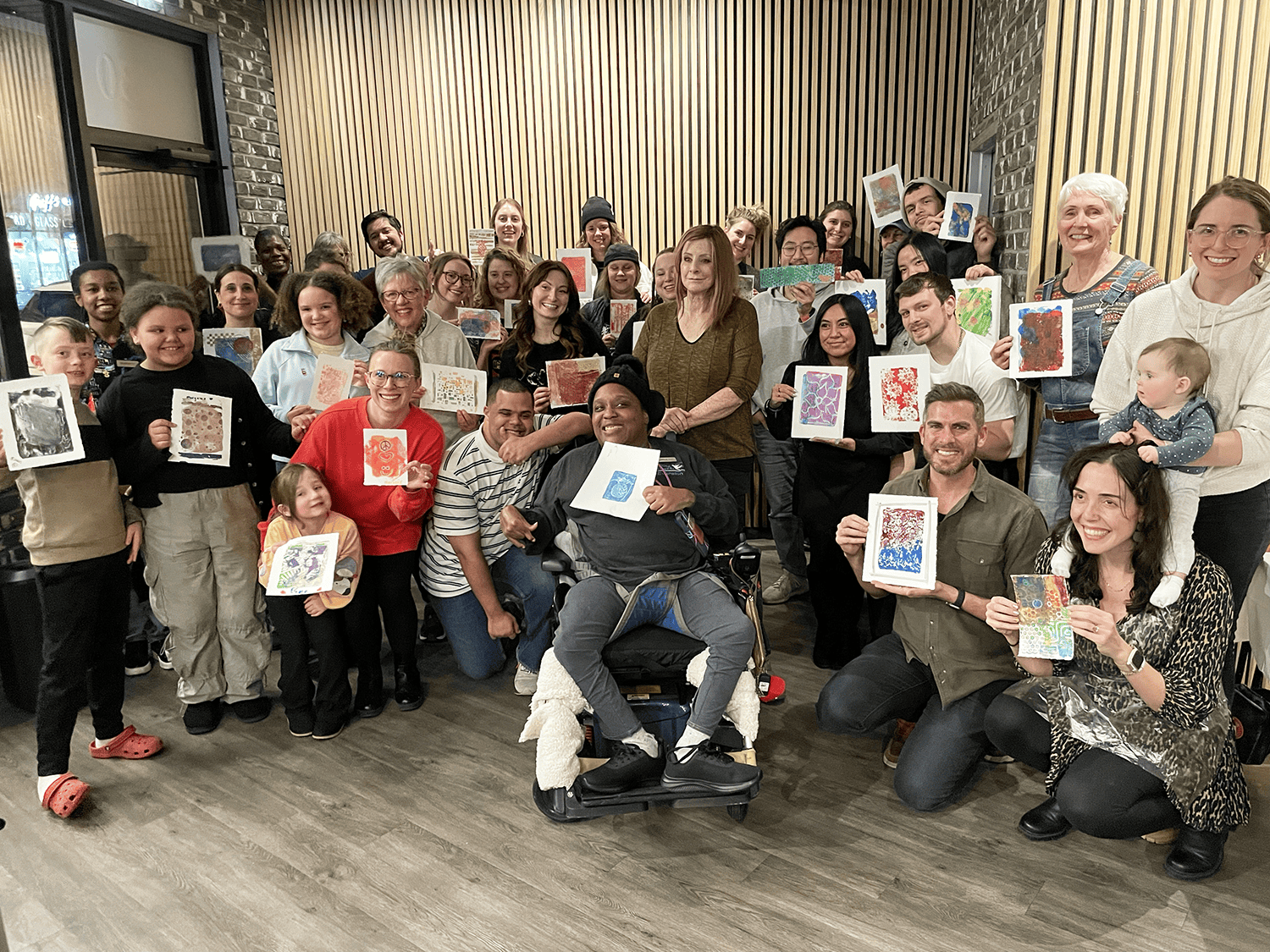 Large group of people all holding up their paintings from the Paint n' Sip class