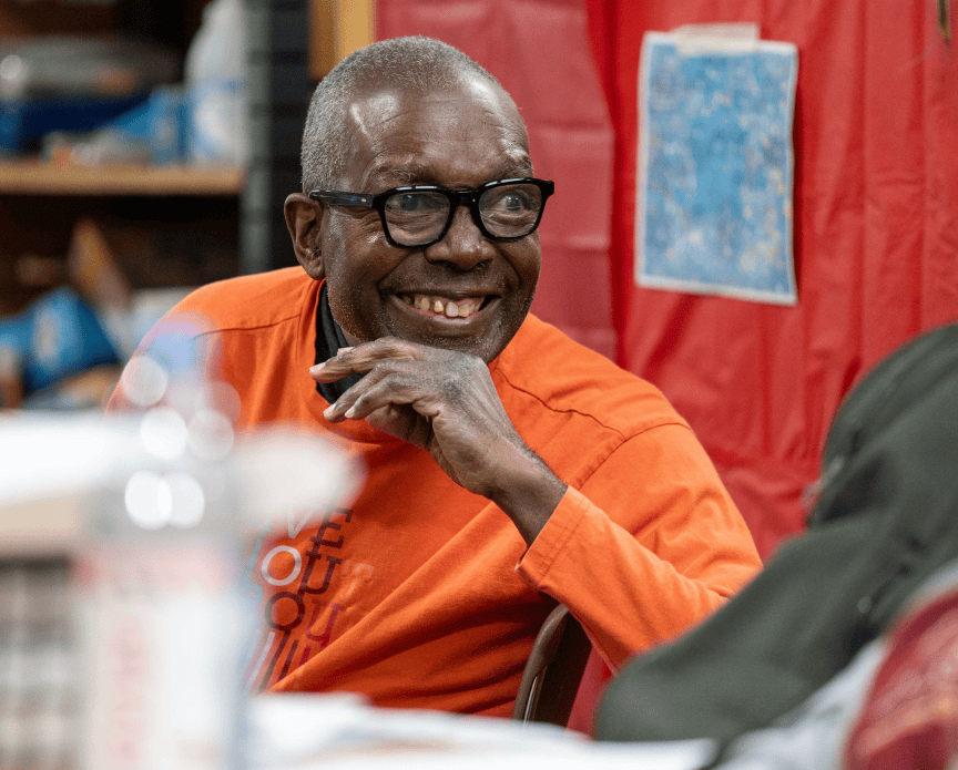 A man in an orange long sleeve and glasses smiline