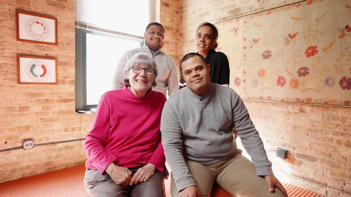 four people sitting and standing while smiling at camera