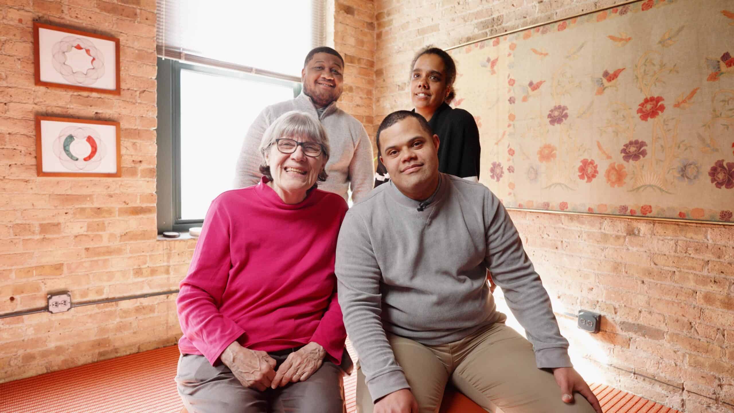 four people sitting and standing while smiling at camera
