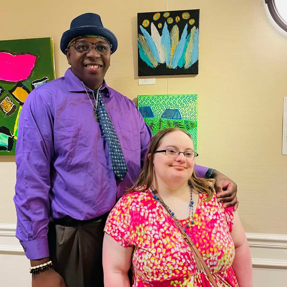 Two artists standing side by side in front of their art for Visibility Arts